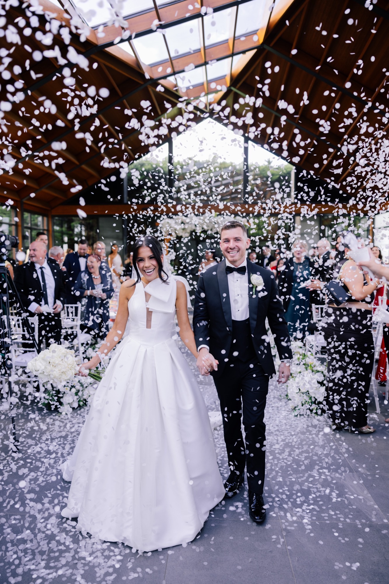 Newlyweds walk through a shower of white confetti in The Green Grove at Marnong Estate
