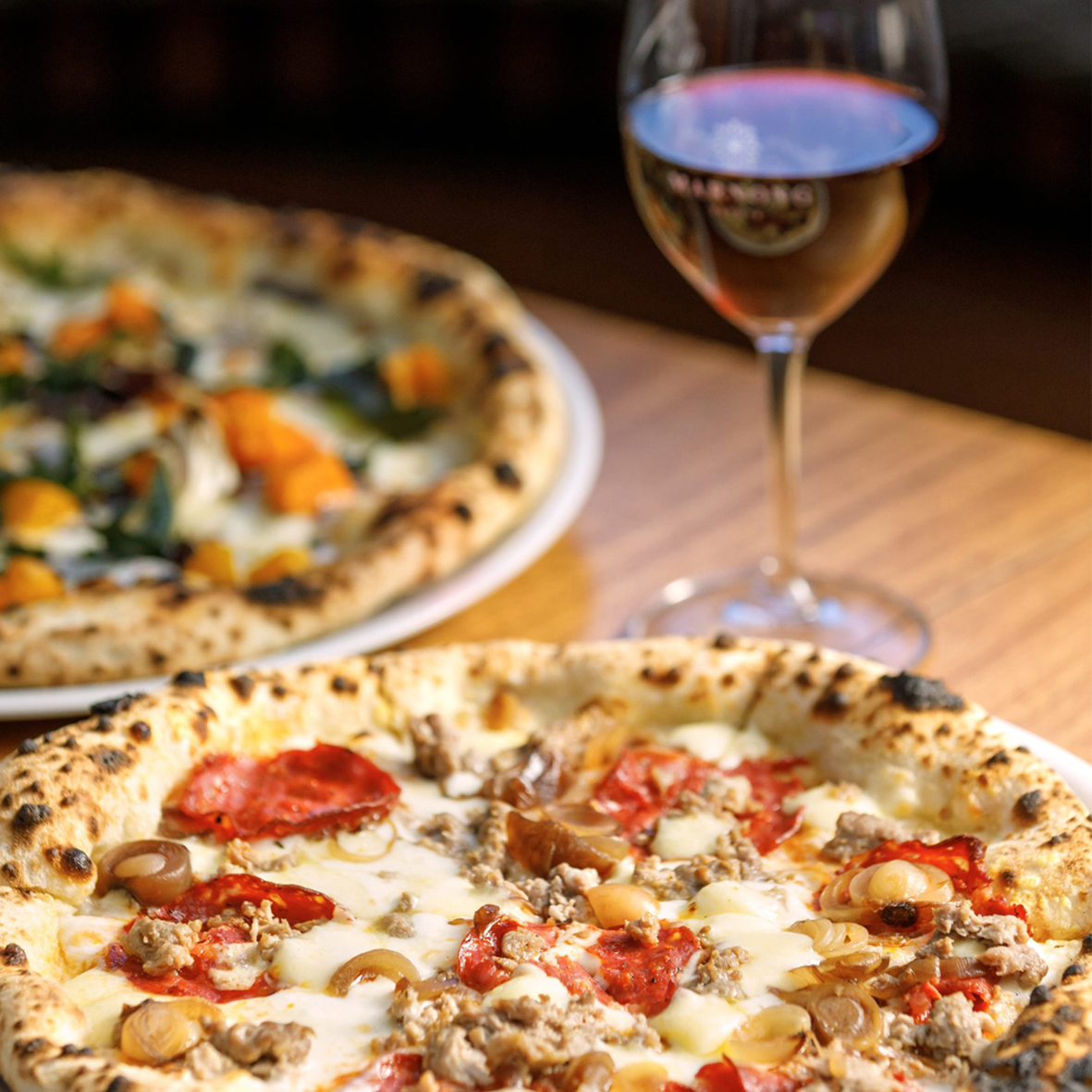 Marnong_Estate_Cucina_Pizza_Boscaiola Two pizzas and a glass of wine on a wooden table