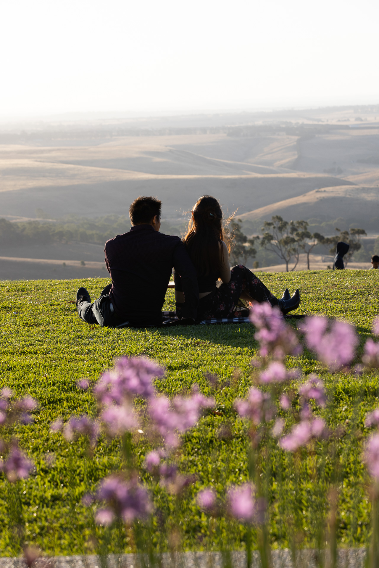 A couple sitting on the main lawn at golden hour, looking across the hills toward the ranges